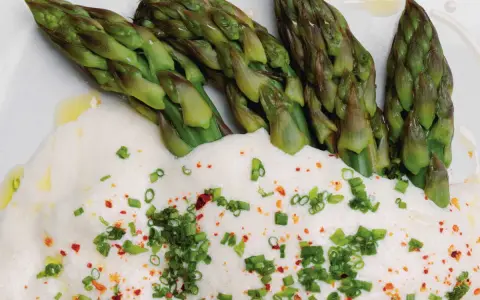 Asperges vertes tendres nappées d'une onctueuse sauce mousseline, parsemées de ciboule et de piment. Un délice printanier.