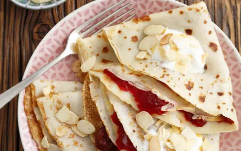Crêpes fines garnies de confiture et de crème, parsemées d'amandes effilées. Une délicieuse recette crêpe sans beurre pour un goûter léger.