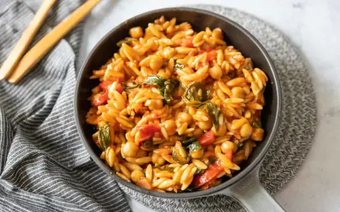 Un plat de cuisson orzo savoureux avec des pois chiches, des poivrons rouges et des épinards dans une sauce tomate.