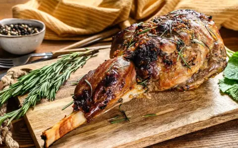 Gigot d'agneau rôti, doré et savoureux, garni de romarin et de moutarde, prêt à être dégusté.