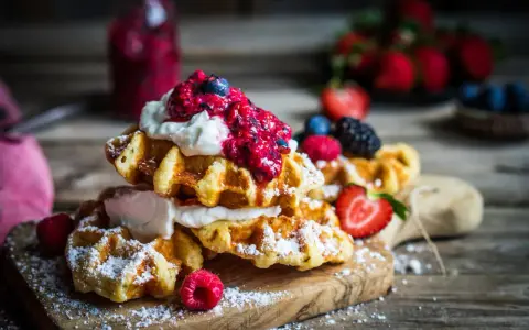 Pile de gaufres traditionnelles garnies de crème fouettée et de fruits rouges, saupoudrées de sucre glace. Un délice pour une recette de gaufre traditionnelle réussie.