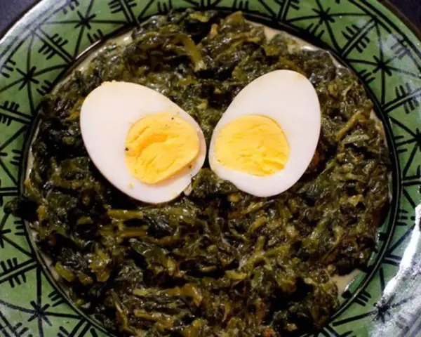 Un plat d'épinards à la crème, parsemé de deux moitiés d'œufs durs, sur une assiette verte décorée.