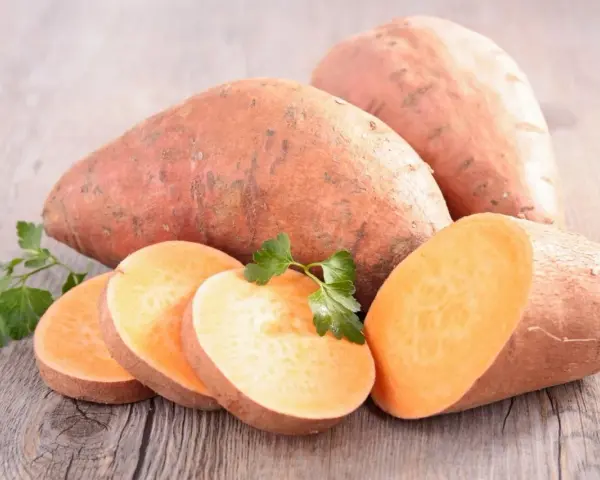 Patates douces entières et tranchées, prêtes à cuire. Une touche de persil frais pour la décoration.