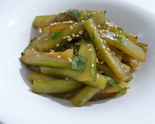 Délicieuse recette concombre cuit, garnie de graines de sésame et de persil frais, servie dans un bol blanc.