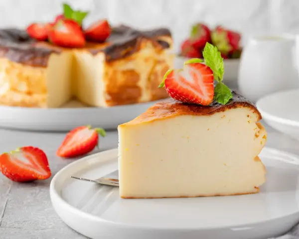 Tranche de gâteau au fromage brûlé, garnie de fraises et de menthe. Un dessert facile qui impressionne, parfait pour toute occasion.