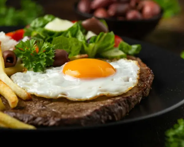 Un plat de steak a cheval savoureux avec un œuf au plat, des frites dorées, du riz blanc et une salade fraîche.