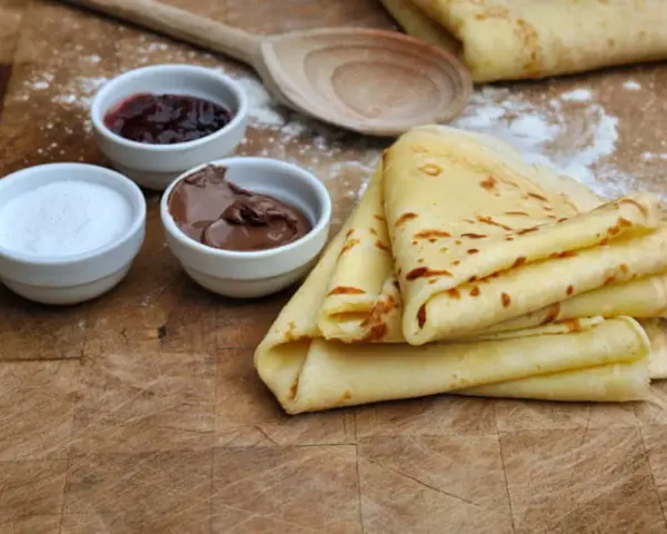 Crêpes dorées empilées, accompagnées de confiture, de pâte à tartiner au chocolat et de sucre. Un délice pour le petit-déjeuner ou le goûter.