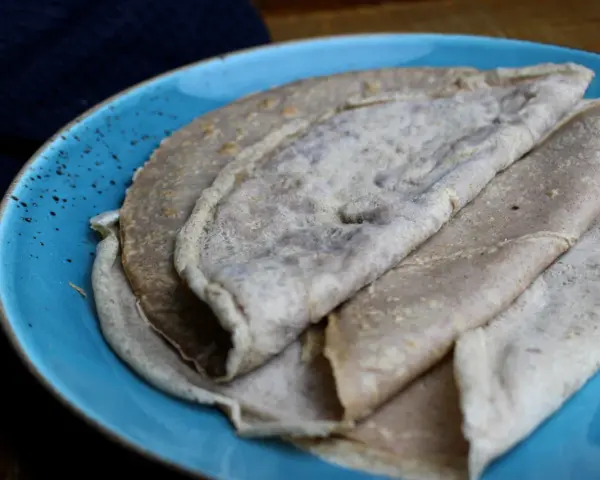 Galettes de sarrasin, naturellement sans gluten, sur une assiette bleue. La farine de blé noir donne cette texture rustique.