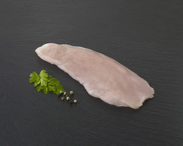 Une escalope de dinde crue, prête à être cuisinée, accompagnée de persil frais et de grains de poivre sur fond sombre.