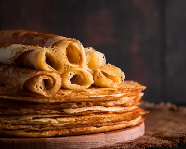 Pile de crêpes dorées, certaines roulées, prêtes à être dégustées. Une astuce pour garder les crêpes au chaud : les empiler ainsi !