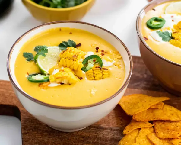 Soupe de légumes crémeuse, garnie de maïs grillé, jalapeños, coriandre et quartiers de citron vert. Servie avec des nachos croustillants.