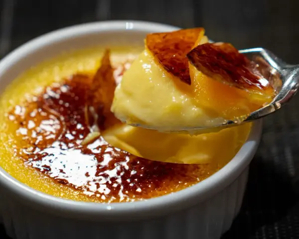 Une cuillère prélève un morceau de crème brûlée, révélant sa texture onctueuse sous une croûte de caramel craquante.
