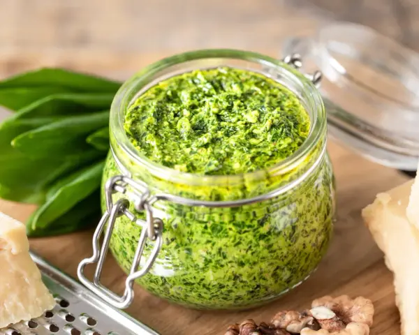 Pesto d'ail des ours dans un bocal, avec des feuilles fraîches, du parmesan et des noix. Une recette maison facile à réaliser.