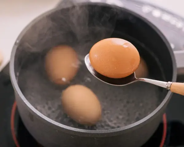 Un œuf mollet est retiré d'une casserole d'eau bouillante à l'aide d'une cuillère. La vapeur s'élève des œufs dans la casserole.