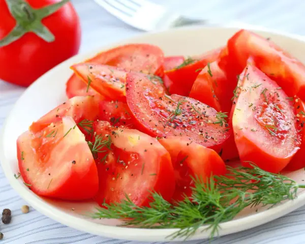 Une assiette de salade de tomates fraîches, assaisonnée de poivre noir et d'aneth. Un délice simple et coloré.