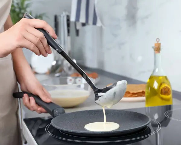 Une louche verse de la pâte à crêpes dans une poêle. On dirait qu'il y a trop de beurre dans la pâte à crêpes, elle est très liquide !