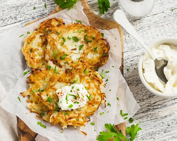 Délicieux rapé de pomme de terre doré, garni de crème fraîche et de persil, prêt à être dégusté avec une touche de paprika.