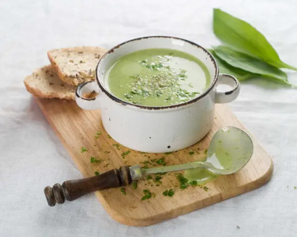 Délicieuse soupe courgette verte, garnie d'herbes fraîches, servie avec du pain grillé et une louche.