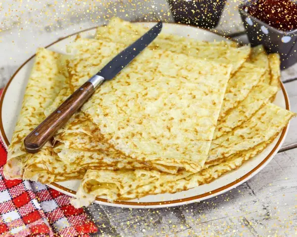 Pile de crêpes bretonnes dorées sur une assiette, prêtes à être dégustées. Un couteau est posé dessus.