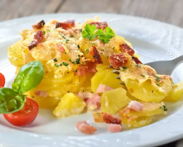 Un délicieux gratin de pommes de terre et lardons, doré au four, servi avec des tomates cerises et du basilic. Un plat réconfortant et savoureux.