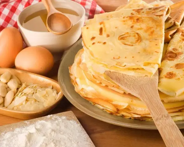Pile de crêpes dorées, ingrédients pour leur origine : œufs, amandes, farine, miel. Un délice sucré.