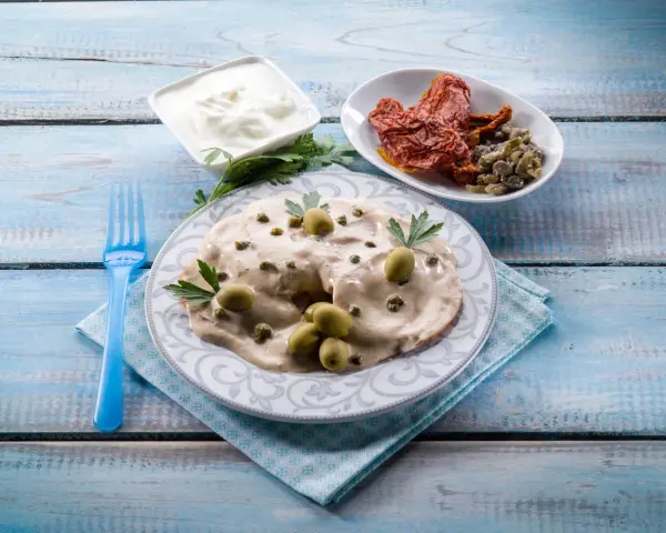 Tête de veau en sauce crémeuse, garnie d'olives et de câpres, accompagnée de tomates séchées et de yaourt.