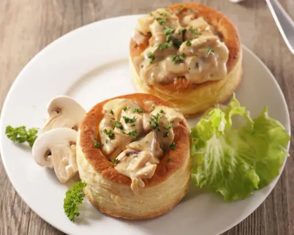 Deux bouchées à la reine garnies d'une sauce crémeuse aux champignons, accompagnées de champignons frais et d'une feuille de laitue.