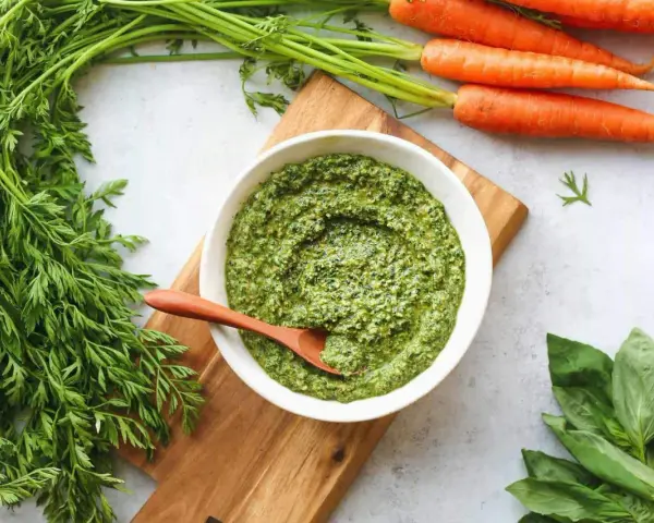 Un bol de pesto de fanes de carottes, avec des carottes fraîches et du basilic à côté.