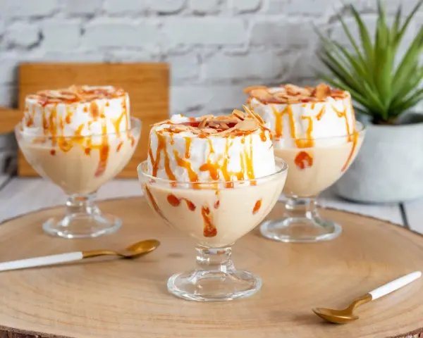 Trois coupes de crème anglaise avec une île flottante meringuée, nappées de caramel et d'amandes effilées.