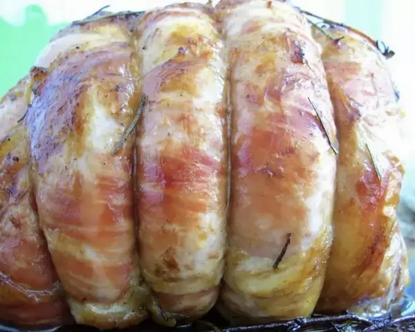 Un délicieux roti de veau, enveloppé de lard et parsemé de romarin, prêt à être dégusté.