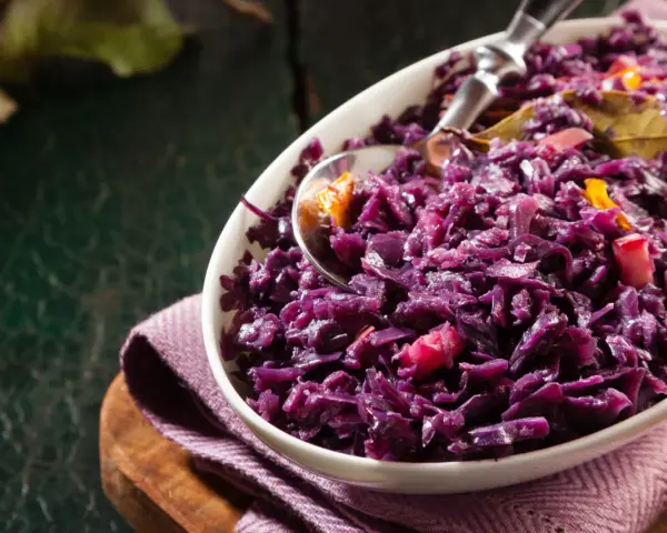 Un plat de chou rouge recette, cuisiné avec des épices et des morceaux de pomme, servi dans un bol blanc.