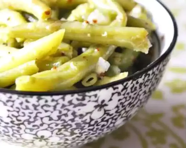 Salade de haricots verts croquants, assaisonnée et parsemée de quelques épices rouges, servie dans un bol décoratif.