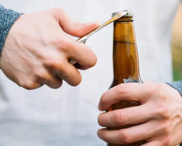 Main gauche tenant une bouteille, main droite utilisant un objet pour ouvrir la bouteille sans tire bouchon.
