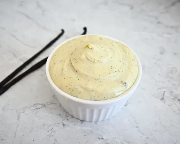 Un bol de ganache chocolat blanc onctueuse, parsemée de points de vanille, avec deux gousses de vanille à côté.