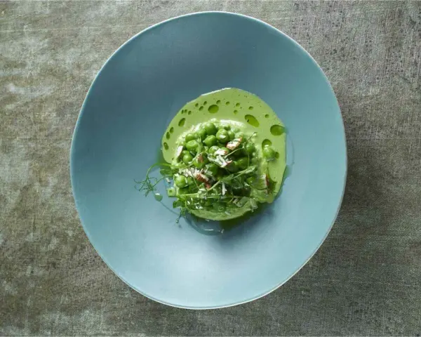 Délicieuse cuisson petit pois frais, servis dans une assiette bleue avec une émulsion verte et des éclats d'amandes.