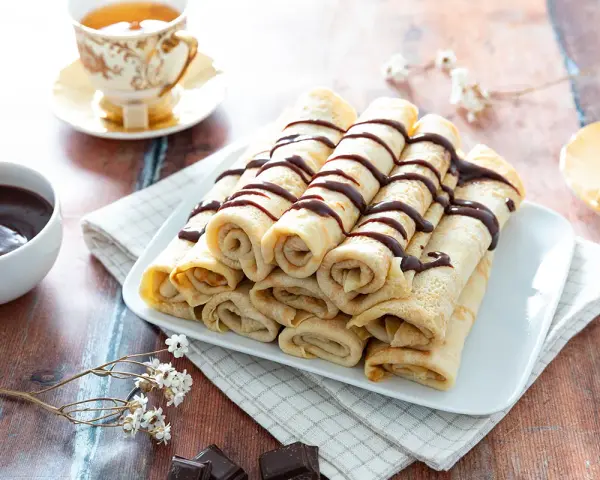 Crêpes roulées, nappées de chocolat, accompagnées d'une tasse de thé. Une recette crêpe raffinée pour un goûter gourmand.