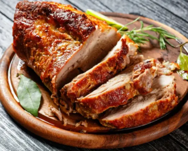 Un rôti de porc au four, coupé en tranches, sur une planche en bois. Le temps cuisson rôti de porc au four moelleux est parfait pour ce plat savoureux.