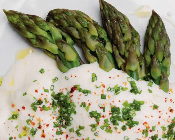 Asperges vertes tendres nappées d'une onctueuse sauce mousseline, parsemées de ciboule et de piment. Un délice printanier.
