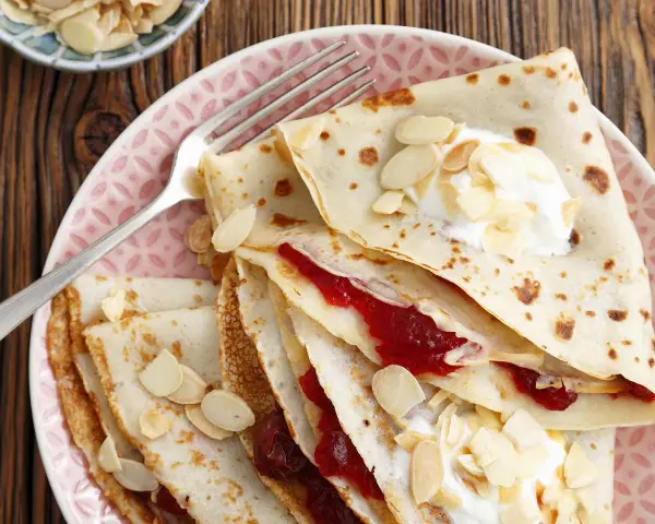 Crêpes fines garnies de confiture et de crème, parsemées d'amandes effilées. Une délicieuse recette crêpe sans beurre pour un goûter léger.
