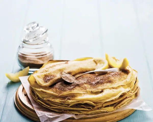 Pile de crêpes au lait entier, saupoudrées de sucre et de cannelle, garnies de quartiers de citron. Un délice simple et gourmand.