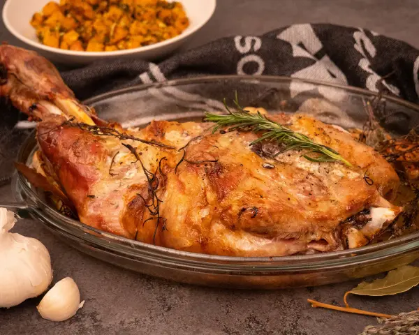 Une succulente épaule d'agneau rôtie à la perfection, garnie de romarin frais, prête à être dégustée.