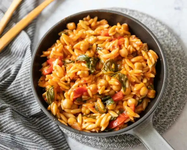 Un plat de cuisson orzo savoureux avec des pois chiches, des poivrons rouges et des épinards dans une sauce tomate.