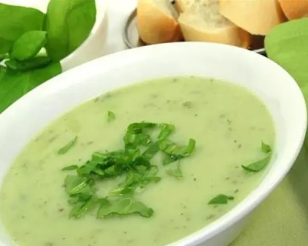 Un bol de soupe à l'oseille crémeuse, garnie d'herbes fraîches, avec du pain en arrière-plan.