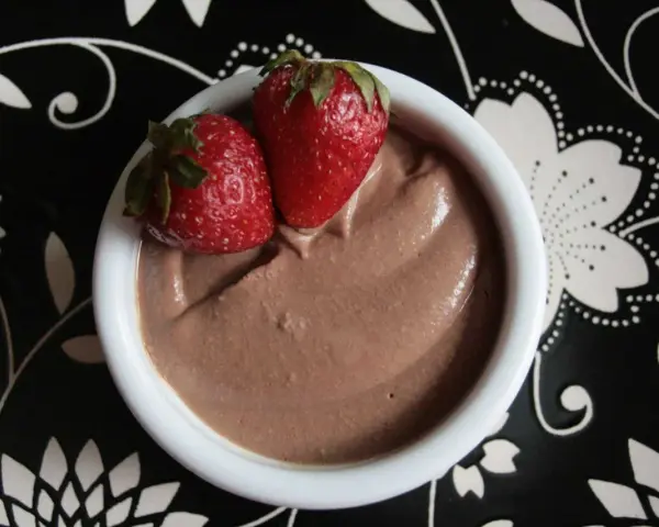 Délicieuse crème au chocolat onctueuse, garnie de deux fraises fraîches, servie dans un bol blanc sur une assiette noire décorée.