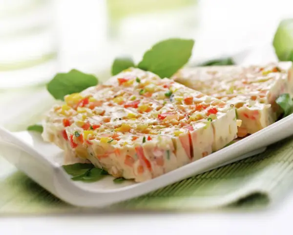 Tranches de terrine de légumes colorée, garnie de feuilles vertes, sur une assiette blanche.