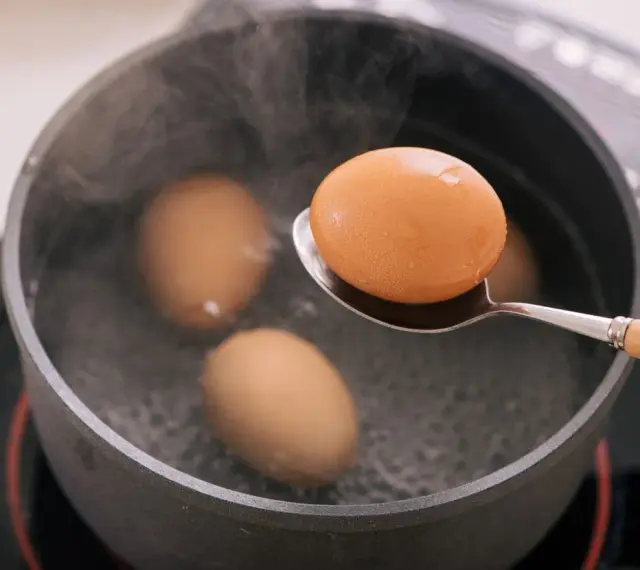Un œuf mollet est retiré d'une casserole d'eau bouillante à l'aide d'une cuillère. La vapeur s'élève des œufs dans la casserole.