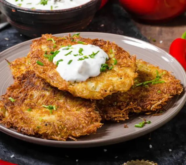 Trois galettes de pomme de terre dorées et croustillantes, garnies de crème aigre et de ciboulette, sur une assiette.