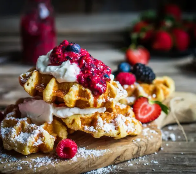 Pile de gaufres traditionnelles garnies de crème fouettée et de fruits rouges, saupoudrées de sucre glace. Un délice pour une recette de gaufre traditionnelle réussie.