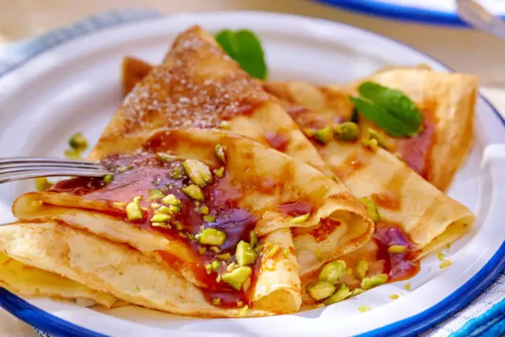 Délicieuses crêpes salées au beurre, garnies de pistaches concassées et d'un coulis rouge. Une touche de menthe apporte de la fraîcheur.