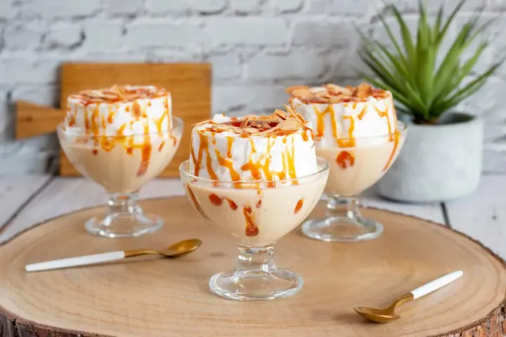 Trois coupes de crème anglaise avec une île flottante meringuée, nappées de caramel et d'amandes effilées.